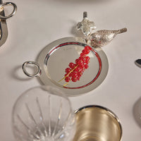 Christofle Vertigo Silver-Plated Bottle/Carafe Coaster with a circular handle, featuring a cluster of red currants resting on its surface and two decorative silver birds nearby.