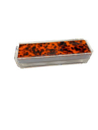 A rectangular, clear acrylic box with a tortoiseshell-patterned lid from Luxe Dominoes, featuring the Rumi Game – Tortoise, isolated on a white background.