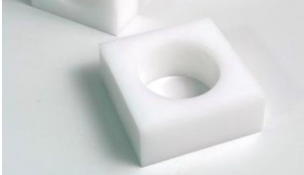 The Lucite Cube Napkin Ring Set of 4 by Tizo features white, square-shaped rings with large circular centers, perfect for modern table decor. One is displayed on a light surface, with another partially visible in the background.