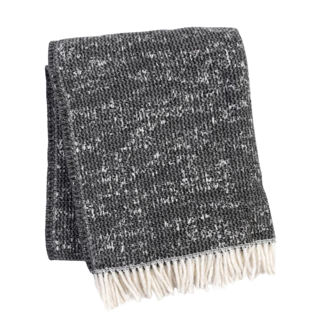 A Soft Idea’s Celestial Throw, in dark gray with a speckled white pattern and fringe, is folded on a white background—blending stylish design with cozy comfort.