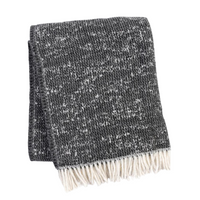 A Soft Idea’s Celestial Throw, in dark gray with a speckled white pattern and fringe, is folded on a white background—blending stylish design with cozy comfort.