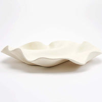 A wavy, white ceramic dish with an irregular, flowing edge sits on a white background. Reminiscent of rippling fabric or an organic shell form, the Celine Raw Blanc Tray by Dumae is hand-crafted to serve as an elegant table accessory—perfectly capturing refined artistry in every detail.