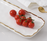 A cluster of fresh cherry tomatoes rests on the PAMPA BAY Portofino Rectangle Tray with gold trim, paired with a gold spoon and white napkin—ideal for oven to table elegance.