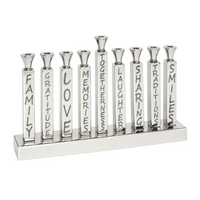 The Mimi Menorah by Inspired Generations is a silver menorah featuring aluminum candle holders, each labeled with words such as Family, Gratitude, Love, Memories, Togetherness, Laughter, Sharing, Traditions, and Smiles—making it a meaningful choice for Hanukkah gifts.