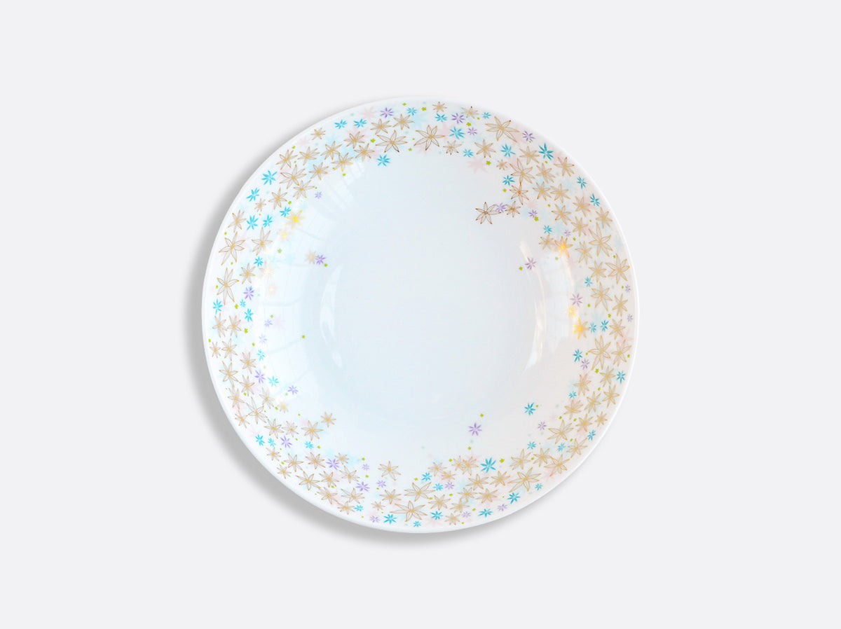 A round white plate from Bernardaud’s Fèerie By Michael Cailloux collection features a gold, blue, and turquoise starburst border, displayed on a plain light gray background.
