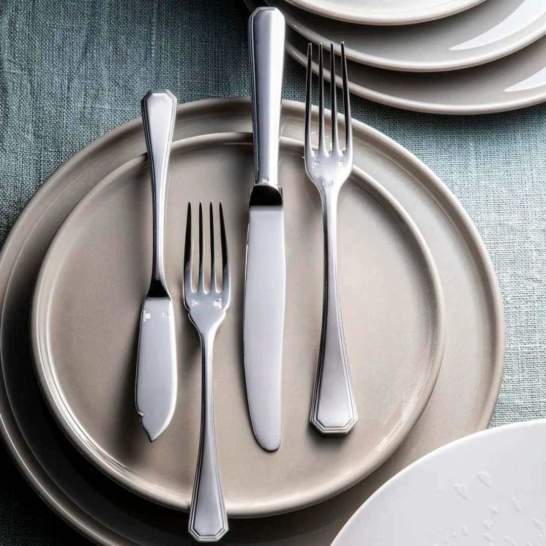 The Christofle America Flatware 5 Piece Setting - Silver Plated is elegantly displayed on stacked beige plates atop a textured teal tablecloth, with extra plates set to the side.