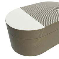 The Lacquer Stripe Box Grey by Von Gern Home is an oval-shaped beige and white box with a lid, featuring a modern geometric striped pattern—ideal for jewelry storage or as a chic accent in contemporary home decor.