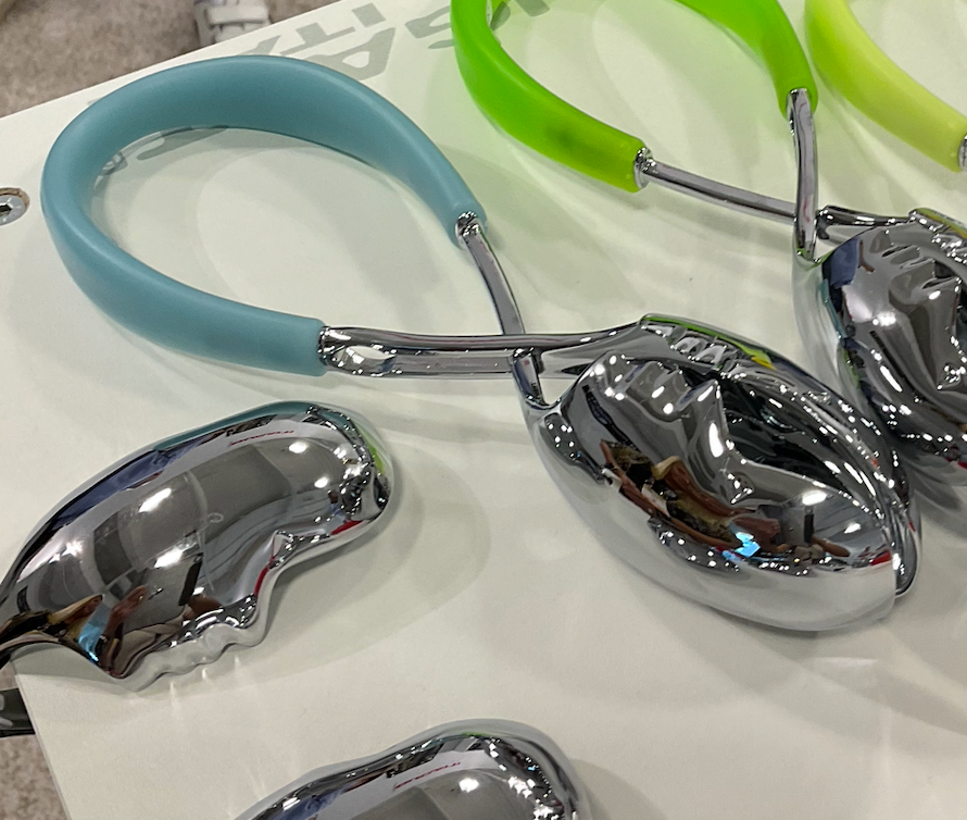 Close-up of the Casa Bugatti KISS Salad Tong, featuring shiny chrome with pastel blue and bright green handles on a white surface—a vibrant table accessory ideal for summer entertaining.