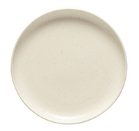 The Costa Nova Pacifica Vanilla Dinnerware is a round, off-white ceramic plate with subtle speckled patterns, shown from above on a white background.