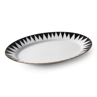 The Punk Dinnerware by Molecot is an oval white Limoges porcelain plate with bold black triangles and a thin gold rim, shown on a white background—a striking example of modern tableware.