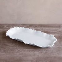 The Beatriz Ball Vida Colette Platter White - Large features a rectangular shape with scalloped, ruffled edges and sits on a brown textured surface against a beige wall—an elegant choice for outdoor entertaining.