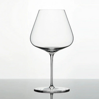 A clear, lead-free Grand Cru Selections / Zalto Burgundy Glass with a wide bowl and thin stem rests on a reflective surface against a plain white background.