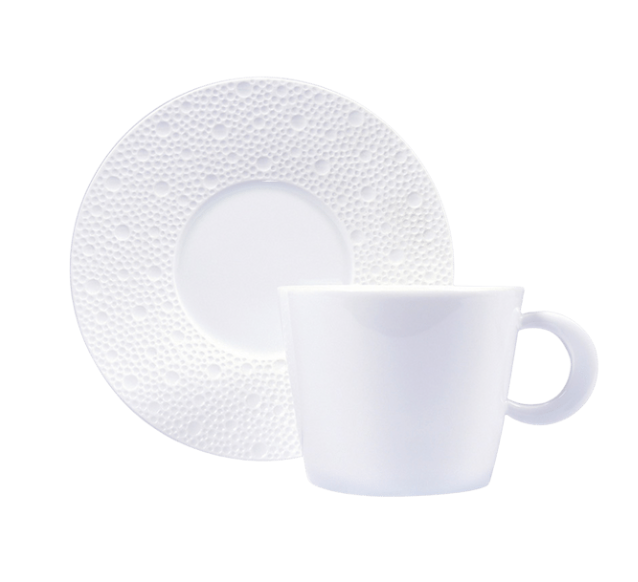 The Ecume White Tea Cup & Saucer by Bernardaud features a simple white ceramic cup with handle and a matching saucer adorned with a textured raised dot pattern around the rim, reflecting minimalist design.