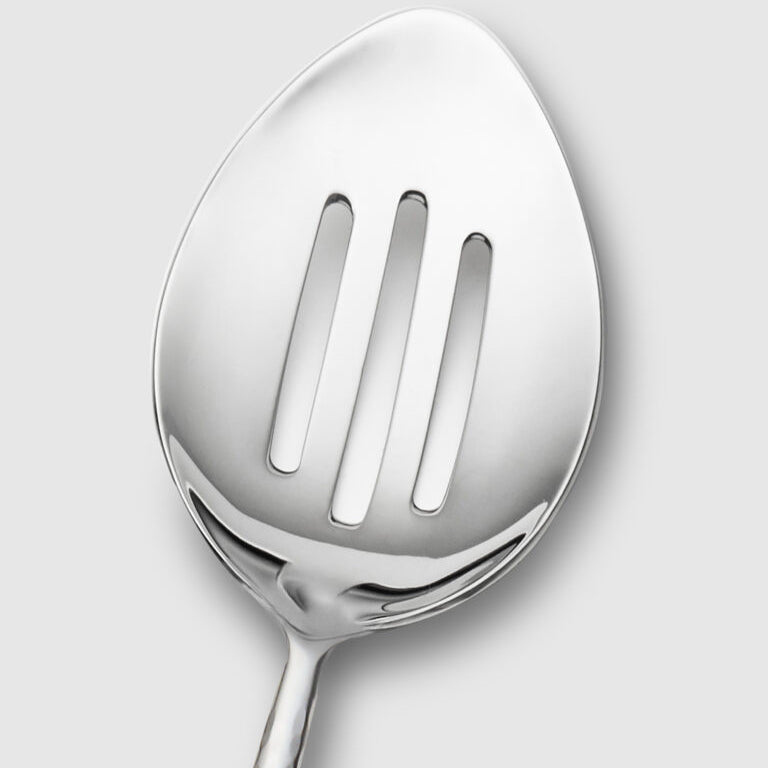 Close-up of the Mary Jurek Alta Slotted Serving Spoon, featuring three elongated slots and a sleek stainless steel finish—a refined addition to your serveware collection, shown against a plain light gray background.