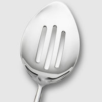 Close-up of the Mary Jurek Alta Slotted Serving Spoon, featuring three elongated slots and a sleek stainless steel finish—a refined addition to your serveware collection, shown against a plain light gray background.