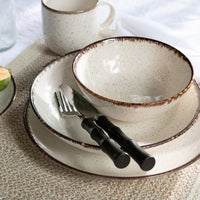 A rustic place setting features a speckled cream bowl, plate, and mug, paired with Blue Pheasant’s Montecito Flatware 5 Piece Setting in Dark Brown, all arranged atop a textured woven placemat.