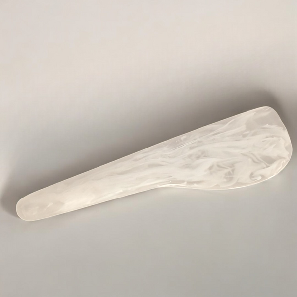The Arila Cheese Knife - White Swirl by Nashi Home is a smooth, elongated knife with a tapered end, shown against a light background—ideal for outdoor entertaining when matched with durable, shatterproof resin decor.
