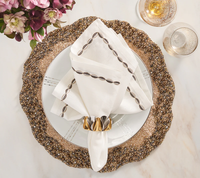 Elegant table setting featuring Kim Seybert's Swag Napkin Gunmetal & Silver Set of 4, a gold beaded charger plate, white plate, two glasses of sparkling drink, and flowers on a marble surface.