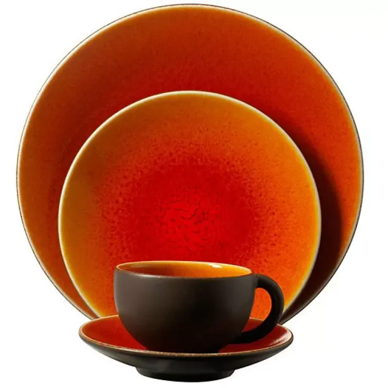 The Jars Tourron Dinnerware Orange set features artisan orange plates and a dark brown cup with an orange interior, displayed on a white background.
