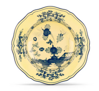 The Ginori 1735 Oriente Italiano Dinnerware Citrino is a decorative porcelain plate with scalloped edges, blue chinoiserie floral motifs, and geometric patterns on a pale yellow background, showcasing classic Italian craftsmanship.