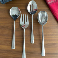The Mary Jurek Alta Deep Garden Vegetable Spoon is arranged on a wooden surface, with a red cloth partially visible in the upper right corner.