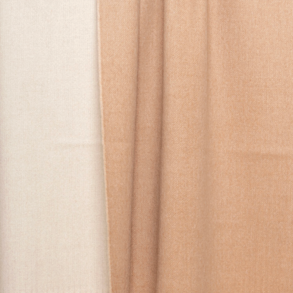 Two panels of fabric drape gracefully side by side; the left panel is a soft beige and the right an inviting ivory, both exuding a gentle sheen. Their silky-smooth texture and subtle vertical folds are evocative of the Reversible Alpaca Throw - Beige & Ivory from Thread & Butter, capturing the understated luxury and refined warmth characteristic of an elegant alpaca throw.