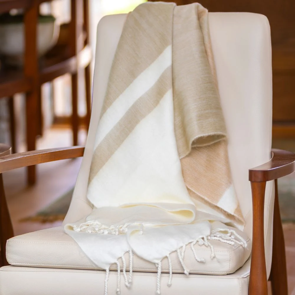 A tan and cream color-blocked Kallpa Collection Alpaca Throw - Tobacco & Wheat with fringe draped over a chair.