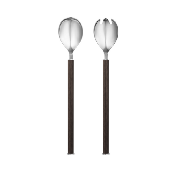 The Bernadotte Stainless and Wood Salad Set by Georg Jensen features two elegant salad servers, each with dark wooden handles and stainless steel heads—one with a solid spoon and the other with a forked design—both standing upright against a white background. These sophisticated serving pieces bring timeless style to your dining experience.