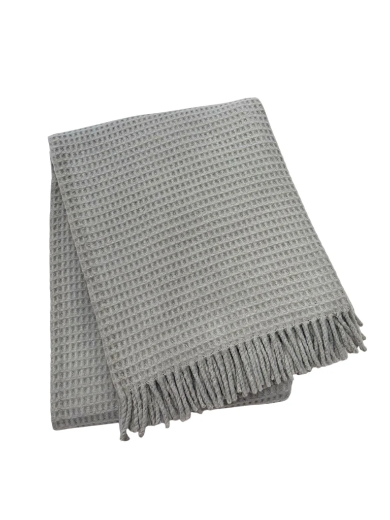 The A Soft Idea Basic Waffle Throw is a folded light gray cotton-acrylic blanket with a waffle pattern and fringed edges, shown on a white background.