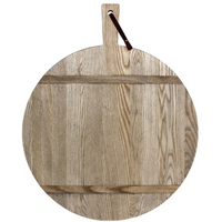 The JK Adams Ash Driftwood Round Serving Board is crafted from ash wood with a natural grain, two support slats, and a handle with dark leather loop—finished in driftwood for rustic charm.
