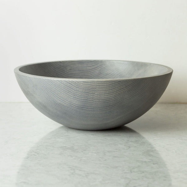 The Peterman Round Wood Bowl Driftwood 15", a large, handcrafted gray oak piece with a smooth matte finish, sits empty on a light-colored reflective surface against a plain white background.