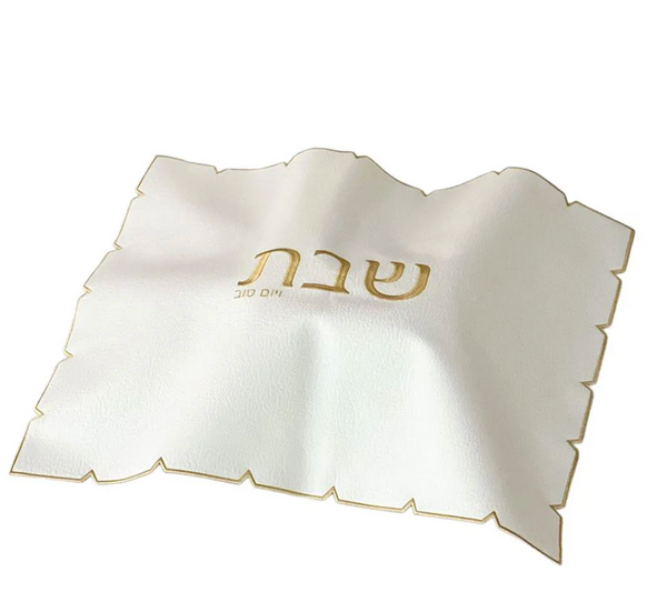 The BT-Shalom White Embroidered Leatherette Challah Cover-Gold features a scalloped, laser-cut edge, gold trim, and "Shabbat" elegantly embroidered in gold at the center.
