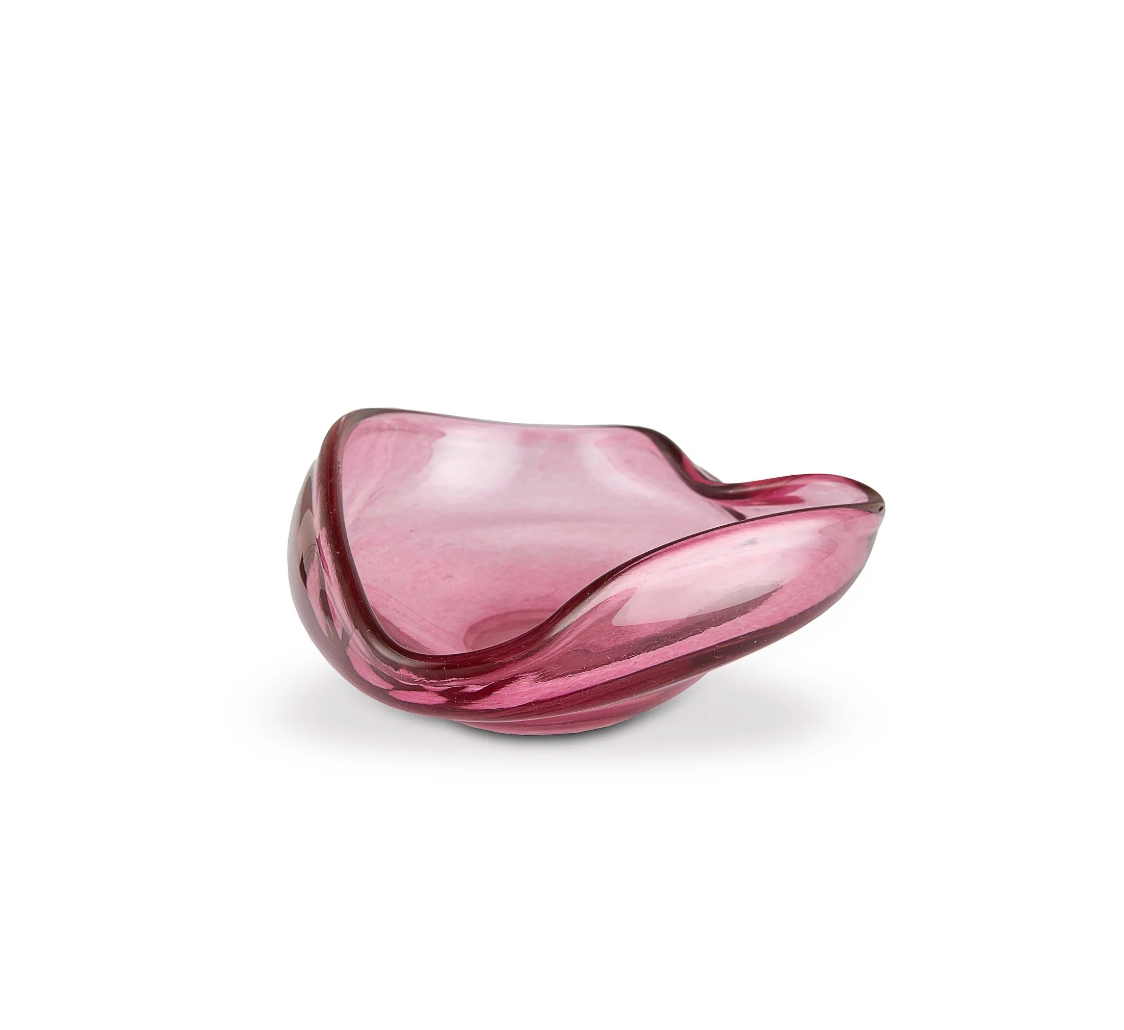 The Aura Small Catchall Bowl by Yakush is a handmade, curved glass piece in pink with smooth edges and a wavy, organic silhouette—crafted from recycled materials. Set against a plain white background, it serves beautifully as a jewelry catchall.