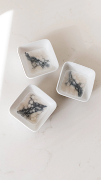 Three Lynn & Liana Serveware Painted Dip Bowls - Marble, filled with a translucent gelatin dessert featuring dark and white swirls, are arranged on a light-colored surface.