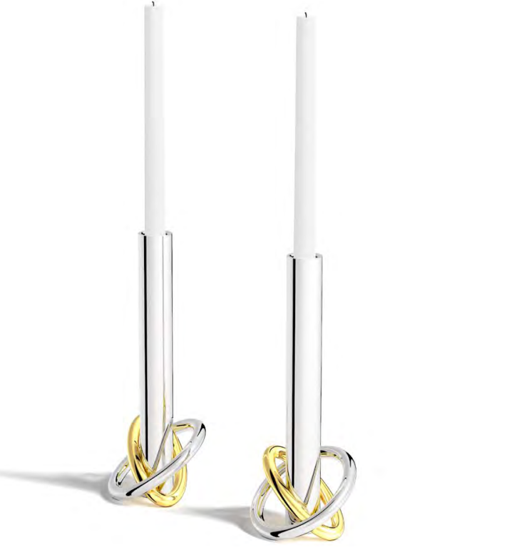 The Anna New York Ring Candle Holder Set of 2 features stainless steel bases with gold, knot-inspired designs, each topped with tall white candles for striking gold and silver contrast against a clean white backdrop.