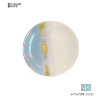 A Marie Daâge Horizon Gold Dinnerware round plate features blue left, white right, and a vertical gold accent. Current Home logo is top left; "Horizon Gold 46" appears bottom right.