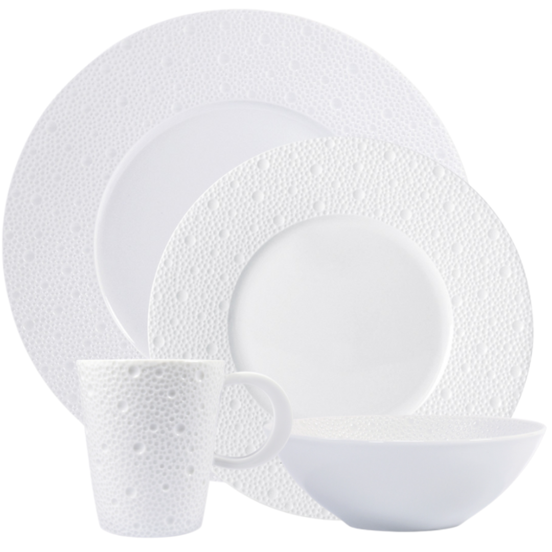 The Bernardaud Ecume White Dinnerware set, made in France, features a textured bubble pattern on the rims and mug exterior. Includes plates, a bowl, and a mug.