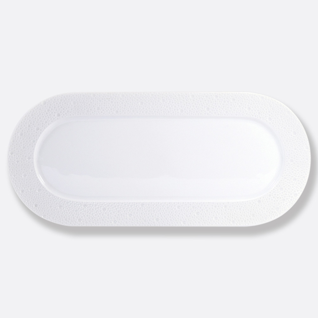 An oval-shaped Ecume White Dinnerware plate by Bernardaud, crafted from white Limoges porcelain with a smooth center and subtly textured raised rim, shown on a light gray background.