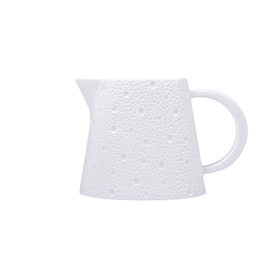 The Ecume White Dinnerware by Bernardaud features a white ceramic pitcher with a textured, dimpled surface, wide base, narrow spout, and curved handle, crafted from fine Limoges porcelain and shown against a plain white background.