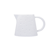 The Ecume White Dinnerware by Bernardaud features a white ceramic pitcher with a textured, dimpled surface, wide base, narrow spout, and curved handle, crafted from fine Limoges porcelain and shown against a plain white background.