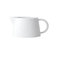 The Ecume White Dinnerware pitcher by Bernardaud features a textured, dimpled ceramic surface with a wide base, curved handle, and pointed spout, all set against a plain white background.