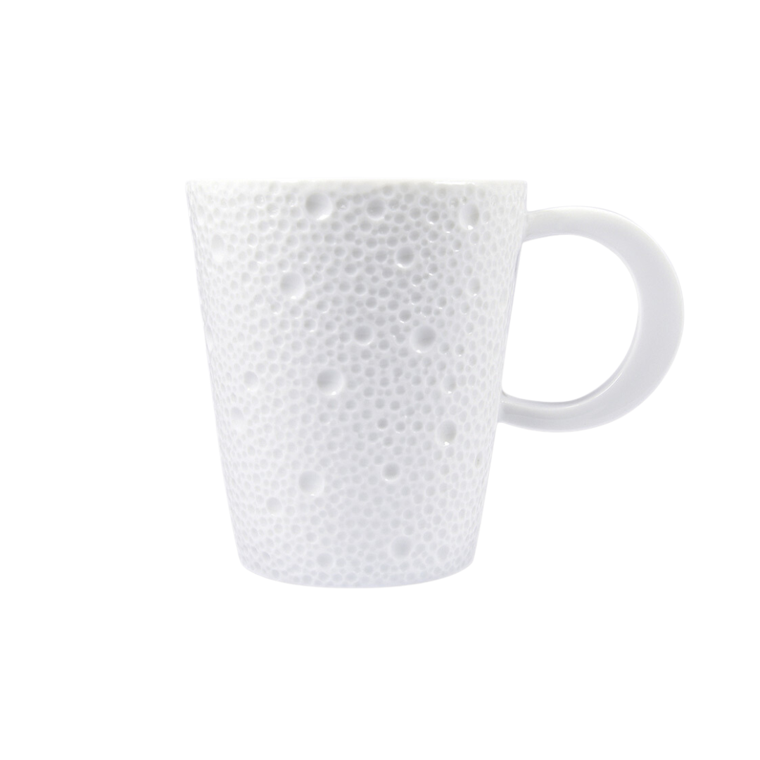 The Bernardaud Ecume White Dinnerware mug is crafted in France from white Limoges porcelain, featuring a large handle and a textured surface with raised dots and bumps, shown against a plain white background.
