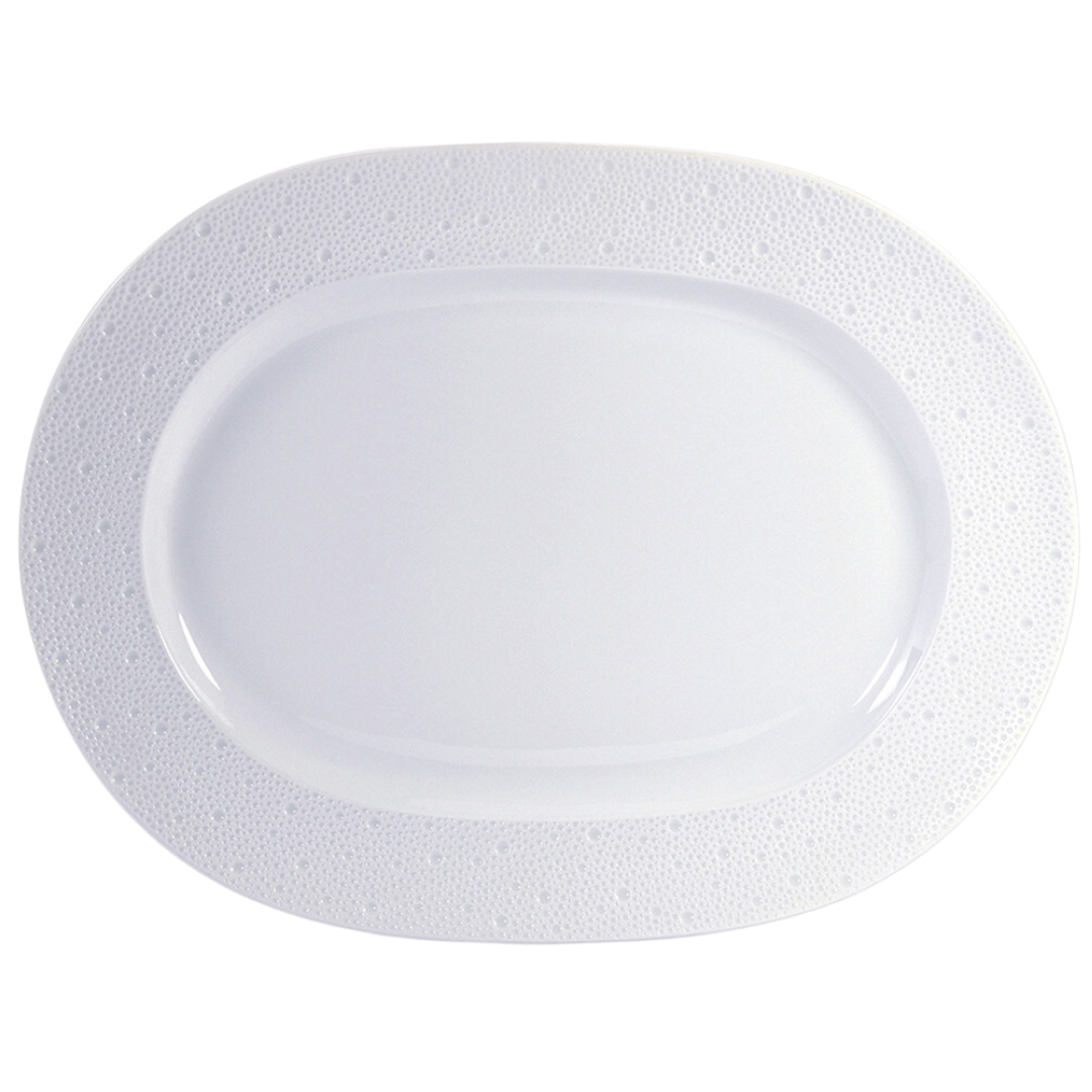 The Ecume White Dinnerware oval platter by Bernardaud is made in France with a subtly textured, dotted rim. Shown on a white background.