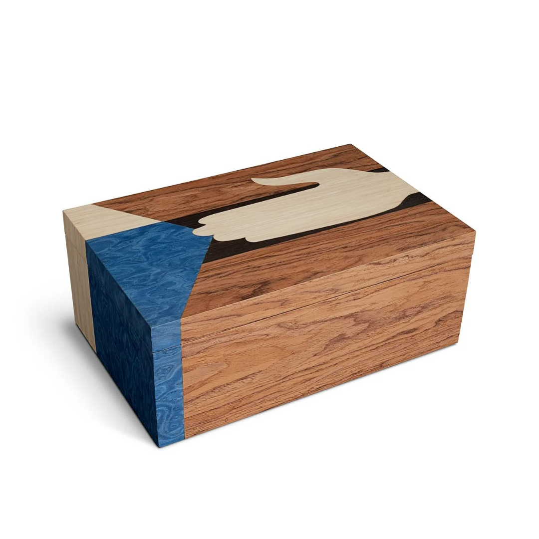 The Edgar Box by L'Objet is a rectangular marquetry box of light and dark wood with an inlaid hand holding a blue triangle on the lid and side—an elegant example of exotic wood craftsmanship.