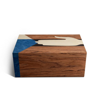 The Edgar Box by L'Objet is a rectangular marquetry box with a smooth finish and a lid featuring art of a hand reaching toward a blue triangle on a brown wood-grain background.