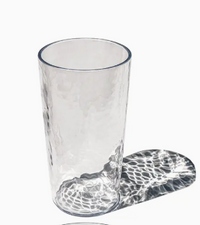 The TarHong Provincial Jumbo Glass - Clear 23oz stands upright on a white surface, casting a patterned shadow to the right. Stylish, durable, and dishwasher safe, it’s perfect for everyday use.
