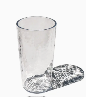 The TarHong Provincial Jumbo Glass - Clear 23oz stands upright on a white surface, casting a patterned shadow to the right. Stylish, durable, and dishwasher safe, it’s perfect for everyday use.