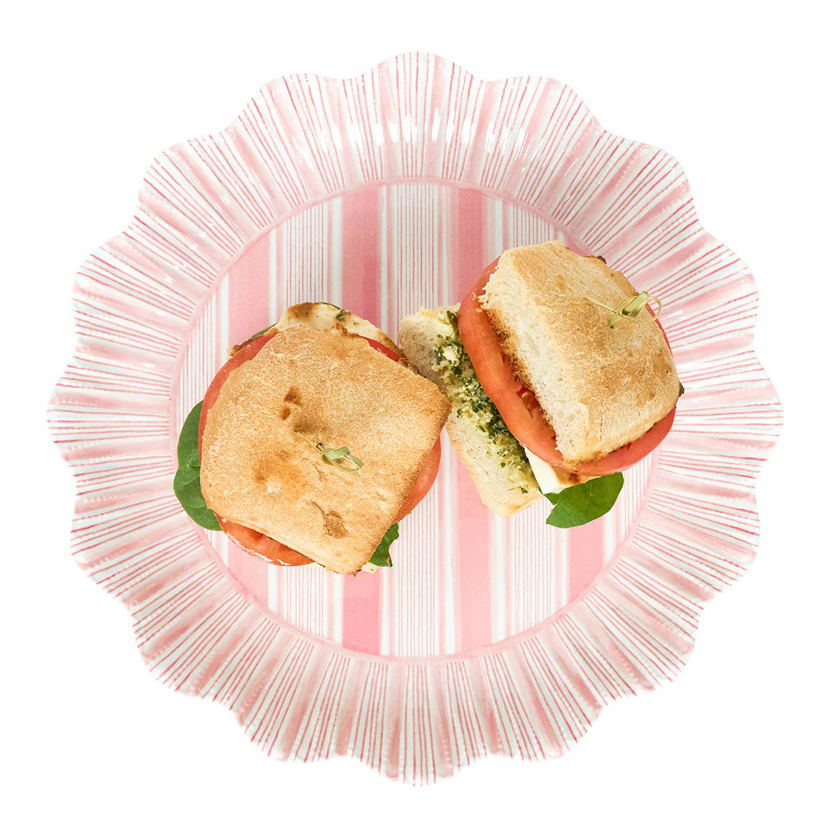 A sandwich with tomato, mozzarella, and greens, cut in half and served on a Juliska Cabana Stripe Melamine Dinnerware plate in coral.