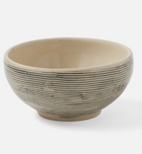 The Blue Pheasant Nolan Dinnerware Black Cream is a round ceramic bowl from an artisanal collection, featuring a smooth beige interior and a ridged, darker exterior, shown on a plain white background.