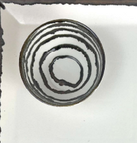 The Michael Wainwright Linea Dip Bowl is a round ceramic bowl with a black spiral on its white interior, shown from above on a white surface with black borders along the left and top edges.